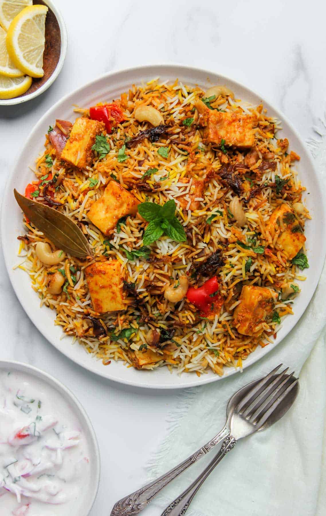 Paneer biryani served in a platter with lemon wedges and raita on the side
