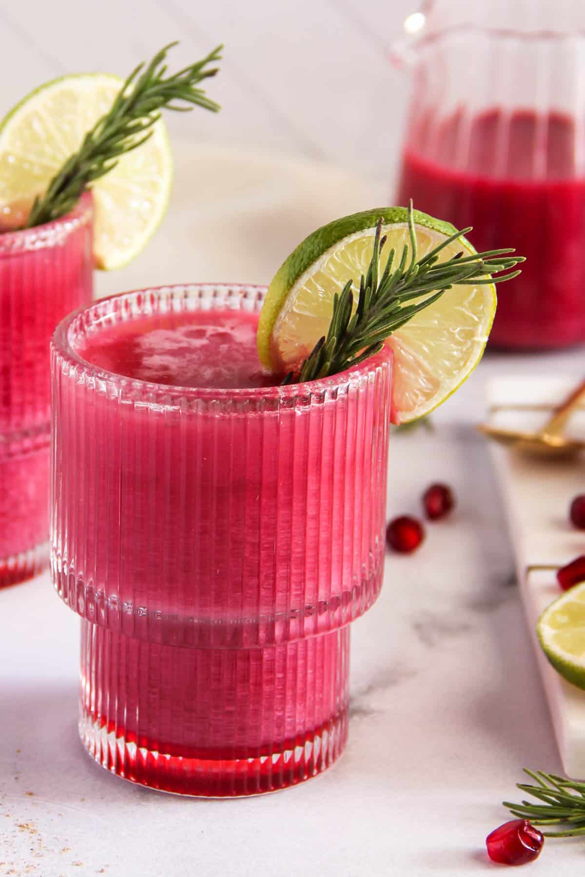 pomegranate rose spritz in a glass with rosemary and lime garnish 
