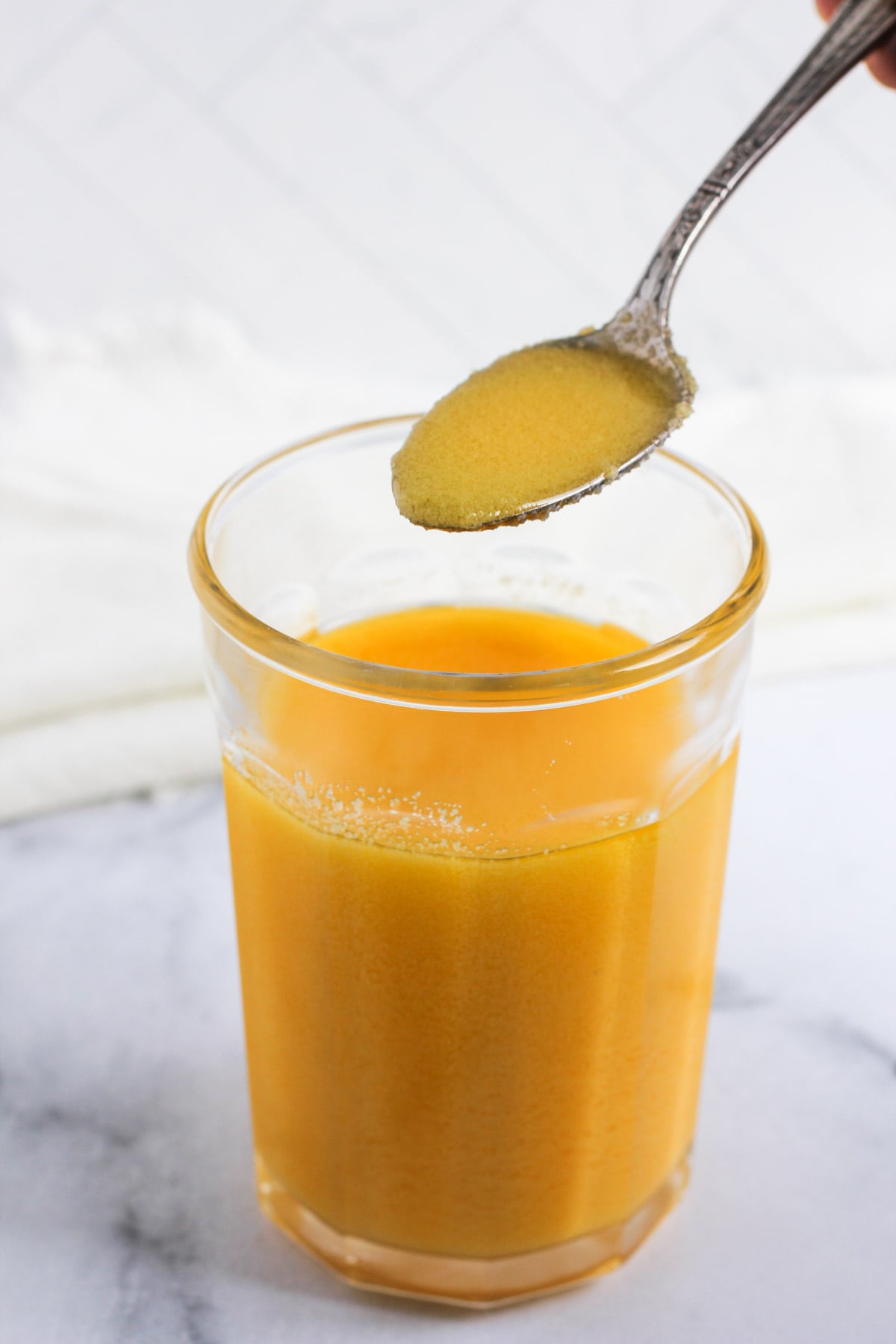 Glass jar with ghee and a spoon showing the grainy textures 