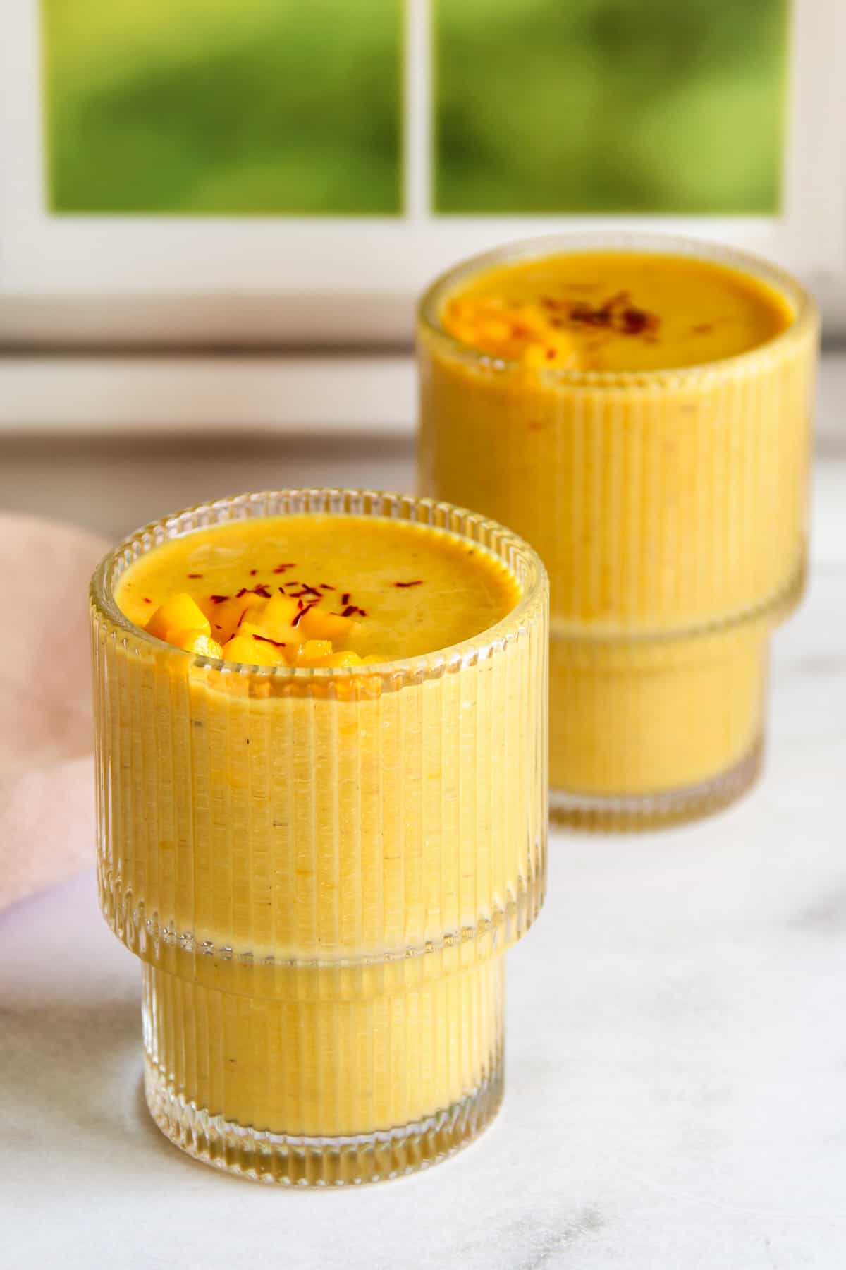 mango thandai served in 2 glasses topped with diced mango and saffron.