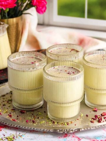 Thandai served in 4 cups garnished with rose petals and pistachios