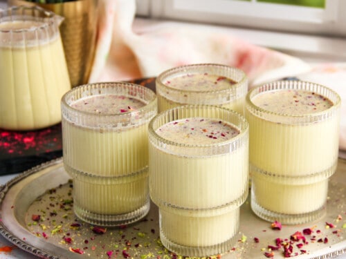 Thandai served in 4 cups garnished with rose petals and pistachios