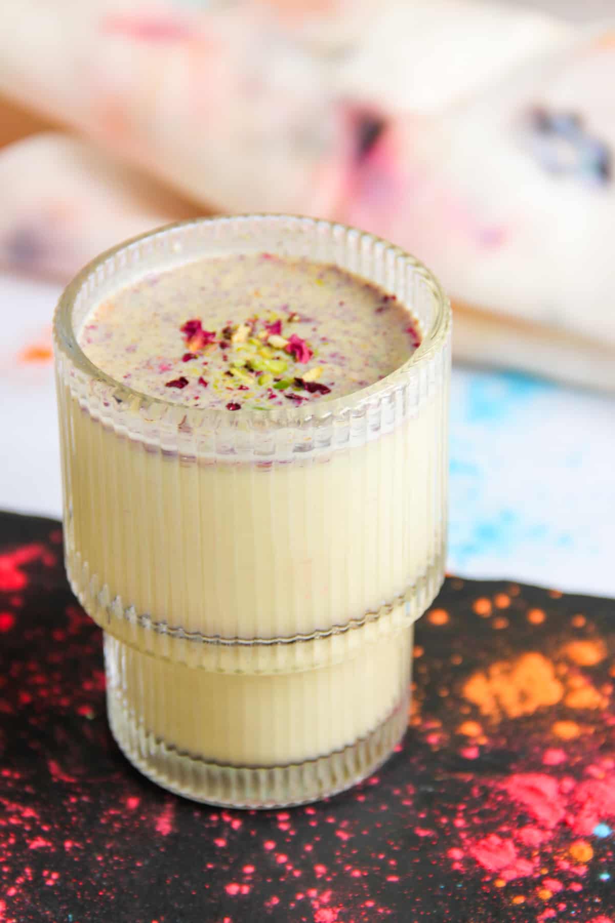 Thandai served in a glass cup garnished with rose petals and pistachios. 