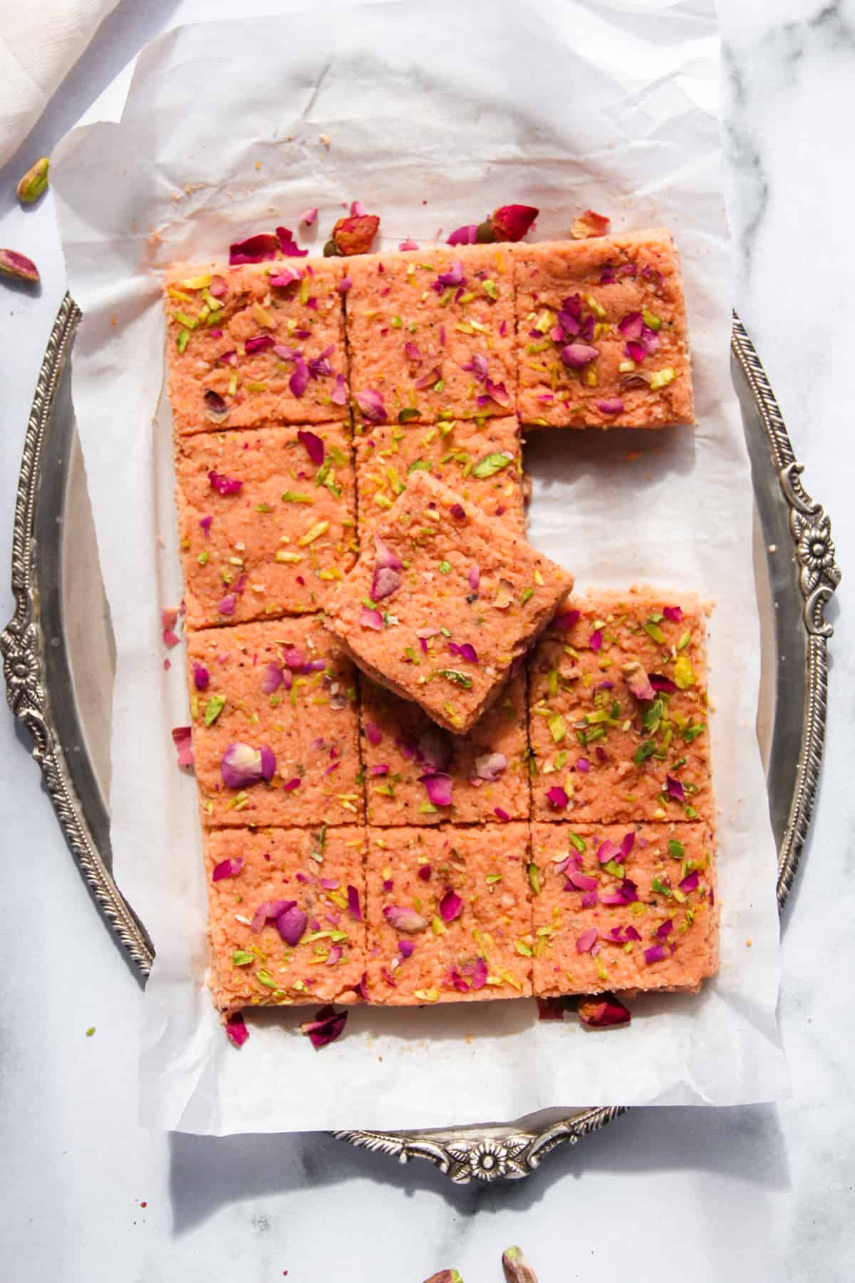 thandai kalakand in a silver platter garnished with dried rose petals and sliced pistachios.
