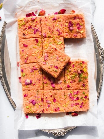 thandai kalakand in a silver platter garnished with dried rose petals and sliced pistachios.