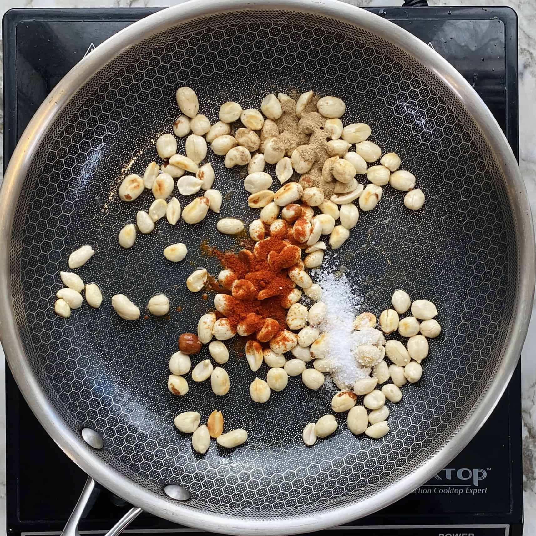 spices added to peanuts in a pan.