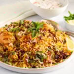 chicken biryani in a serving platter with raita bowl on the side,