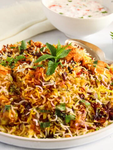 chicken biryani in a serving platter with raita bowl on the side,
