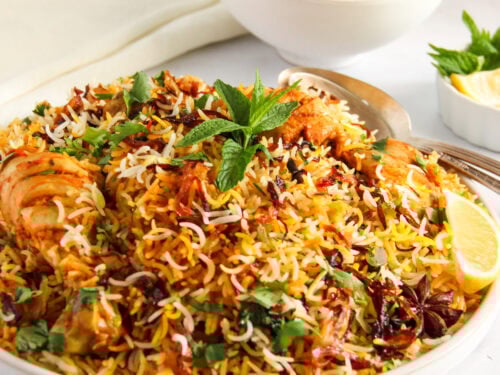 chicken biryani in a serving platter with raita bowl on the side,