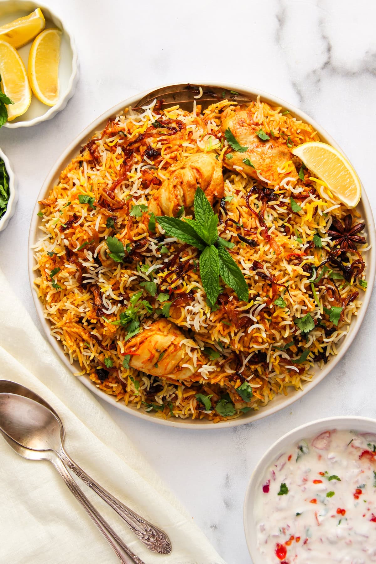 Chicken Biryani served in a white platter with lemon wedge and raita on the side.