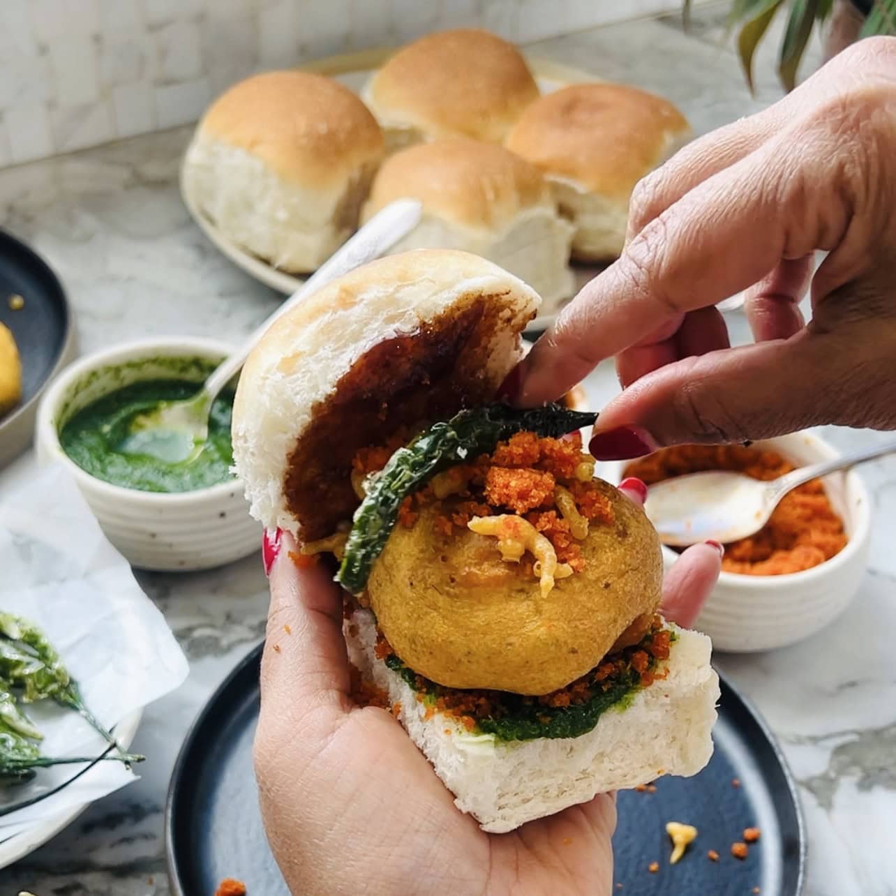 adding chura and fried green chili on vada pav