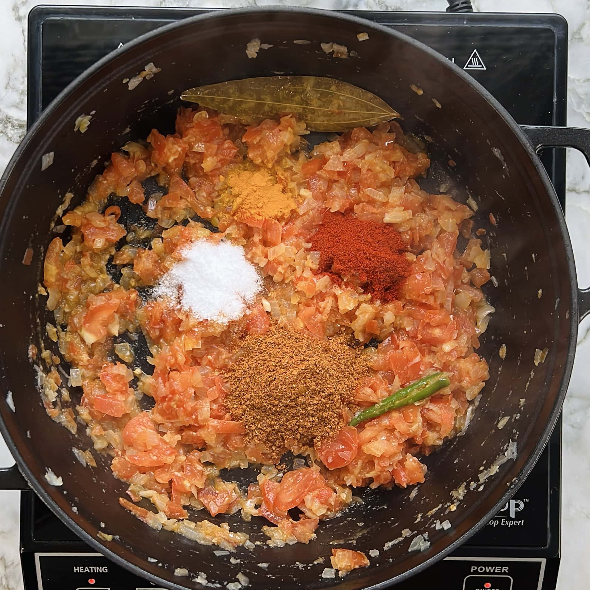 dry spices added to sauteed onions and tomatoes in a pan 