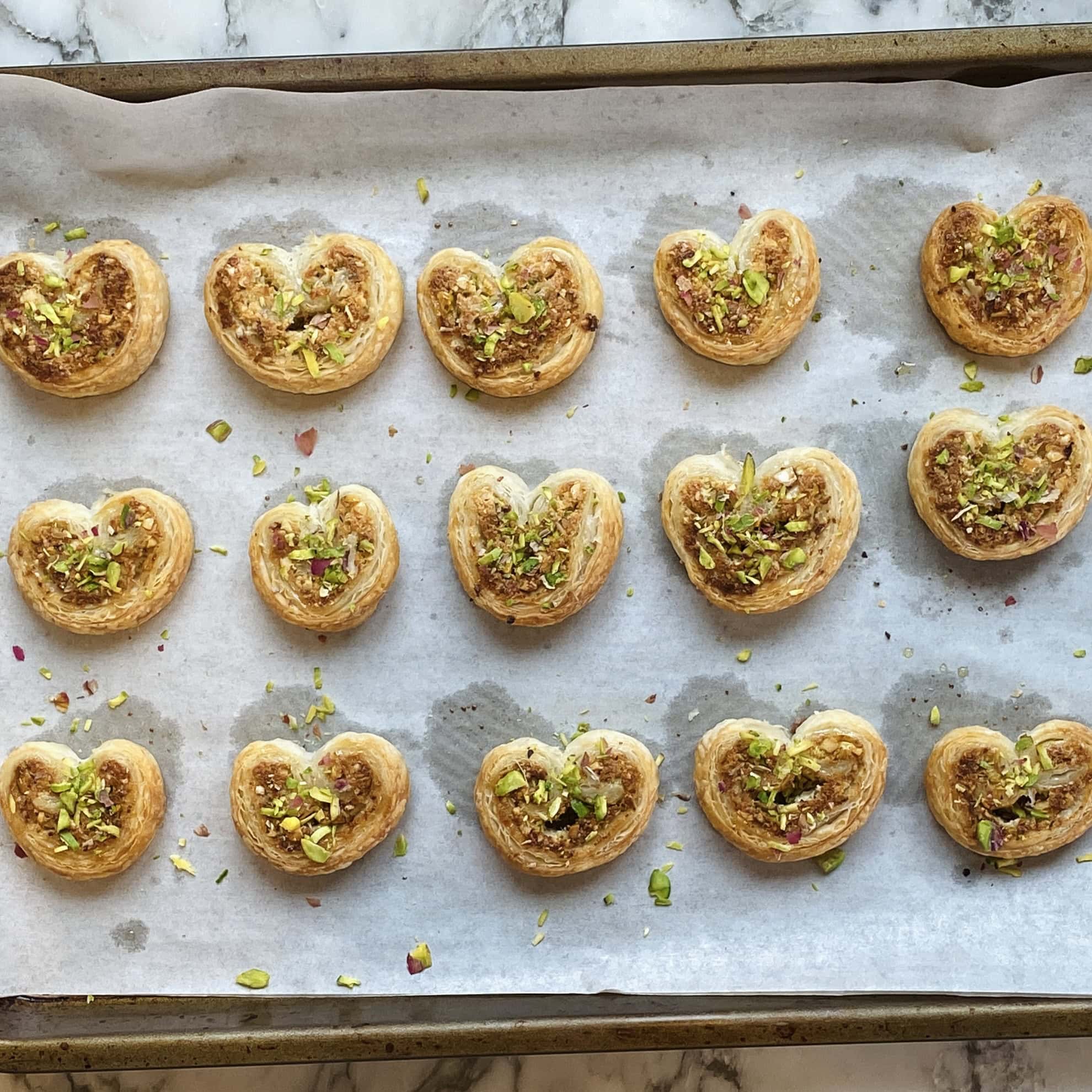 gujiya bites on a baking tray garnished with pistachios. 