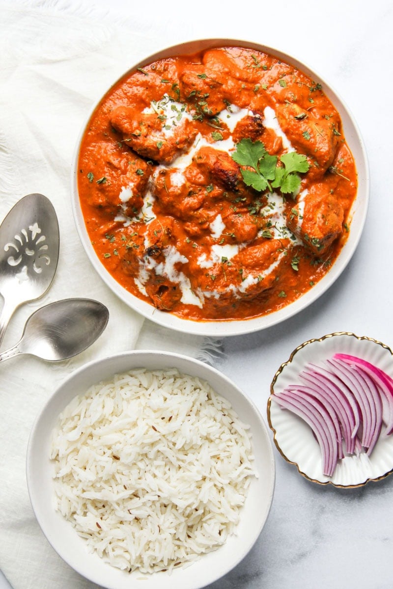 chicken tikka masala served with jeera rice and sliced red onions.
