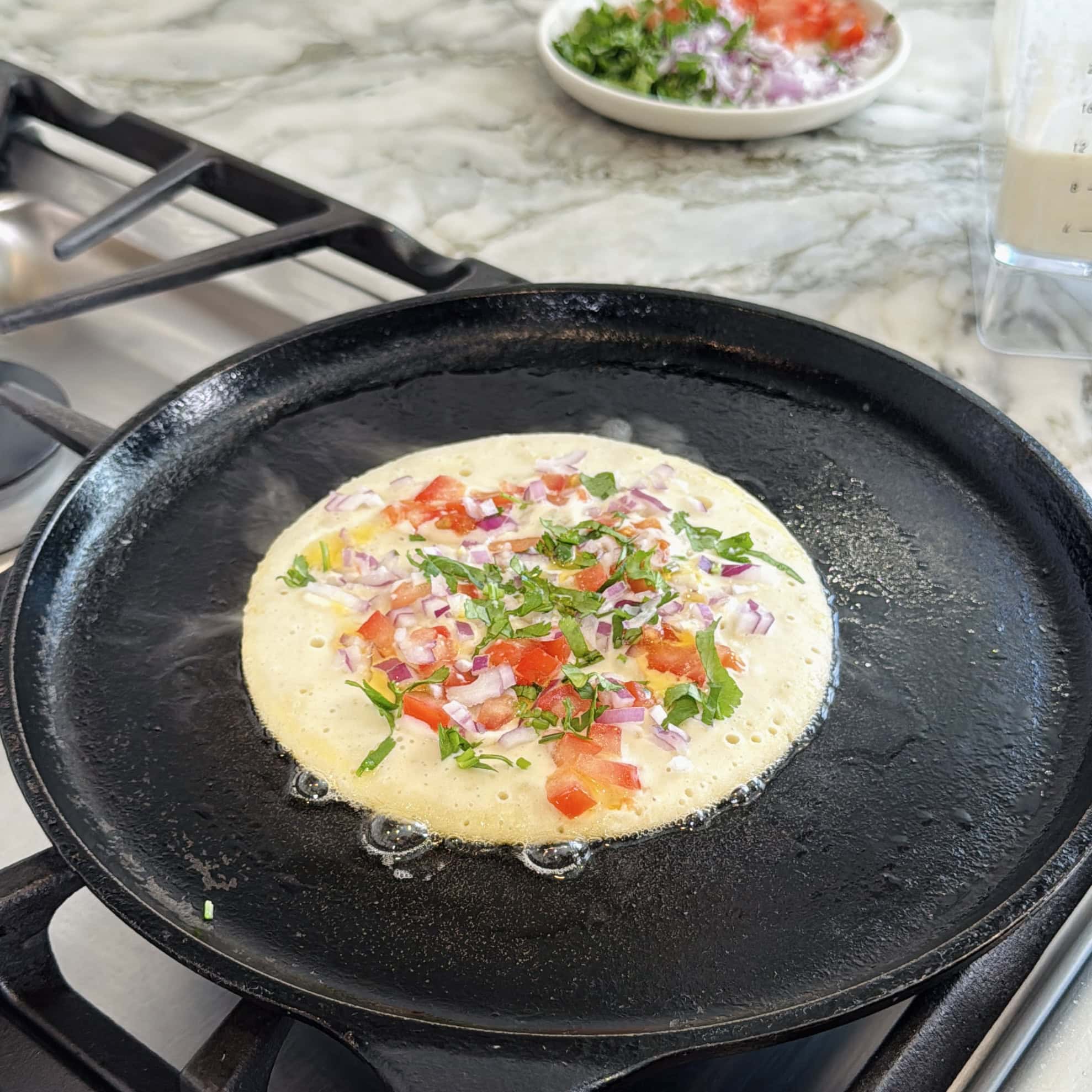 uttapam on a cast iron pan with onions, tomato and cilantro. 
